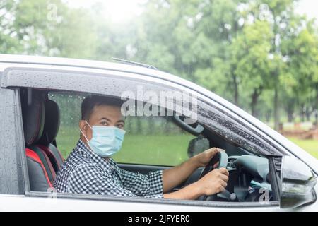 Guida sicura durante la giornata di pioggia. Persone asiatiche indossare maschera e guida mentre piove. Effetto svasato obiettivo Foto Stock