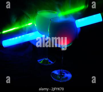 Due cocktail fumosi con tubo al neon e laser verde, su sfondo scuro. Uno dei bicchieri accende lentamente l'alcol all'interno. Foto Stock