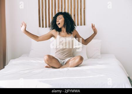 Concetto di umore positivo del mattino. La giovane donna africana ha avuto un buon sonno svegliarsi e divertirsi a casa o in albergo Foto Stock