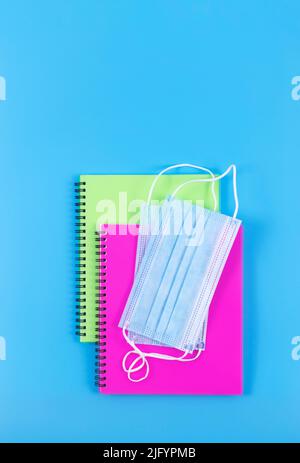 Due copybook a spirale con maschere facciali su sfondo blu. Vista dall'alto. Nuovo concetto normale. Foto Stock