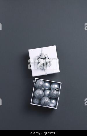 Confezione regalo aperta con decorazioni in argento metallizzato con albero di Natale su sfondo grigio. Vista dall'alto, spazio di copia. Foto Stock