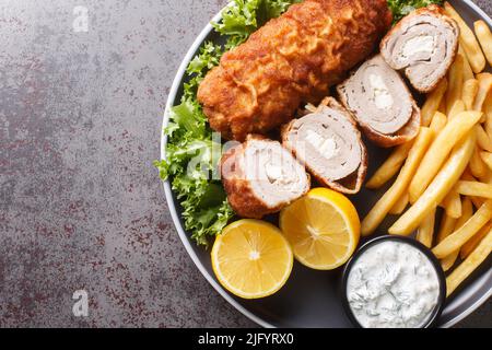 Filetto di carpetta arrotolato serbo Karageorge Schnitzel con patatine fritte e salsa tartara da vicino in un piatto sul tavolo. Vista dall'alto orizzontale Foto Stock