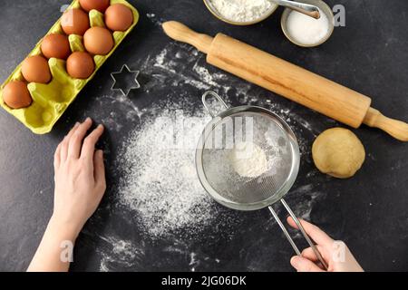 mani con setacciatore setacciare la farina sul tavolo da cucina Foto Stock