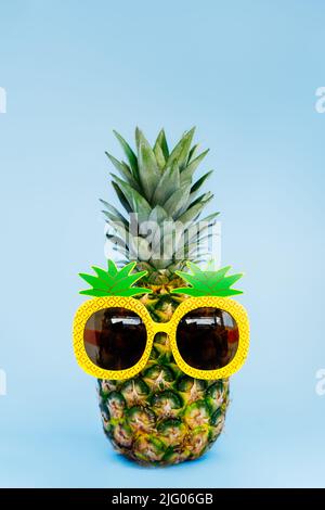 Ananas divertente in un bicchiere di ananas a forma di sfondo verticale blu. Estate in stile tropicale sull'atmosfera della spiaggia. Frutta esotica. Resort vacat Foto Stock