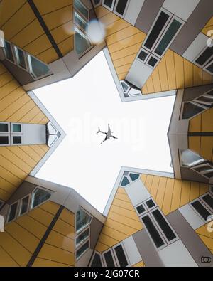 Un piccolo angolo di silhouette in aereo nel cielo limpido visto attraverso le Cube Houses a Rotterdam, Paesi Bassi Foto Stock