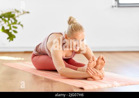 donna che fa yoga e seduta in avanti curva a casa Foto Stock