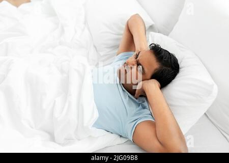 annoiato uomo indiano sdraiato a letto e chiudere le orecchie Foto Stock
