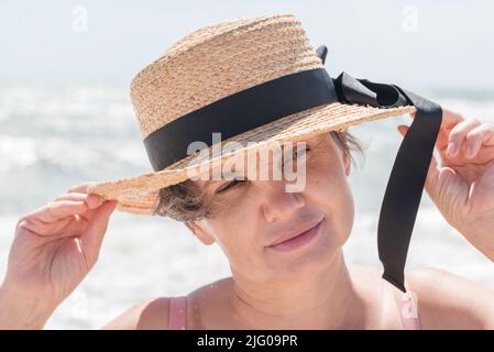 Ritratto di donna dai capelli grigi in un boater con un nastro nero filosoficamente guardando qualcosa con poco sorriso.concetto di femminilità. Foto Stock