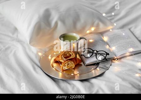 croissant, tè matcha, libro e bicchieri a letto Foto Stock