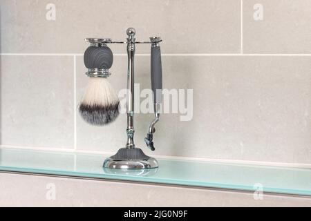 Una spazzola e un rasoio da barba su un supporto cromato su uno scaffale da bagno Foto Stock