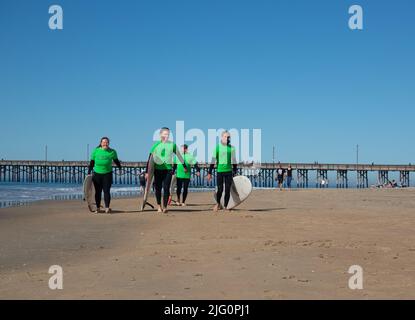 Quattro giovani bagnini con cime verdi che trasportano tavole da surf camminando orgogliosamente lungo la spiaggia a Newport Beach California USA Foto Stock