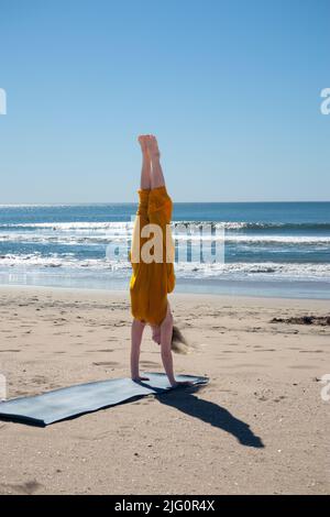 Donna in giallo che fa un palco yoga nella spiaggia California meridionale USA Foto Stock
