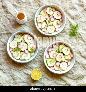 tre piccole ciotole rotonde con ravanello e cetrioli insalata leggera estiva, sfondo tessile verde, vista dall'alto Foto Stock