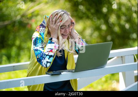 donna emotiva senior con laptop che effettua videochiamate e gesturing attivo, comunicazione online Foto Stock