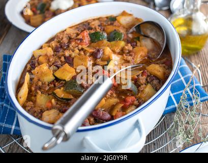 Pasto sano di famiglia con uno stufato di carne tritato, cavolo, verdure e fagioli di rene. Servito in pentola sul tavolo da cucina Foto Stock