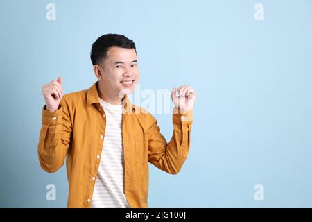 L'uomo asiatico LGBTQ con camicia gialla in piedi su sfondo blu. Foto Stock