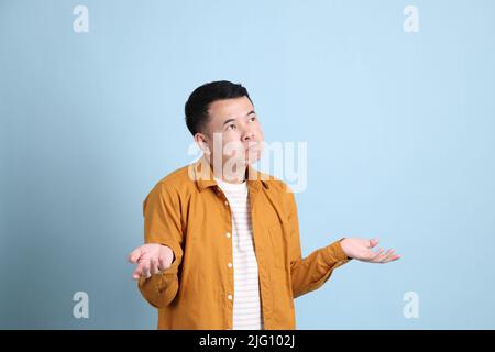 L'uomo asiatico LGBTQ con camicia gialla in piedi su sfondo blu. Foto Stock