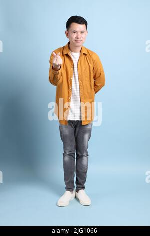 L'uomo asiatico LGBTQ con camicia gialla in piedi su sfondo blu. Foto Stock