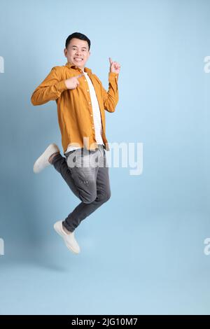 L'uomo asiatico LGBTQ con camicia gialla in piedi su sfondo blu. Foto Stock