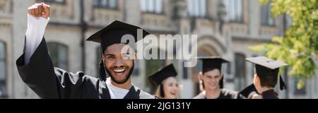 Eccitata bachelor afroamericano in cap mostrando sì gesto nel parco, banner Foto Stock