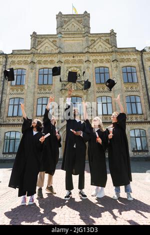 Bachelor interrazziali positivi con diplomi che lanciano tappi vicino all'università all'aperto Foto Stock