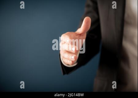 Primo piano di un uomo d'affari che offre la sua mano in stretta di mano o saluto su sfondo blu. Con spazio di copia sul lato sinistro dell'immagine. Foto Stock