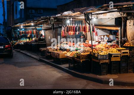 Tbilisi, Georgia - 28 marzo 2022: Vista sul mercato notturno della città di frutta a Tbilisi. Il venditore stanco si è fatto fuori di notte nel mercato. Mercato della frutta e dei dolci Foto Stock