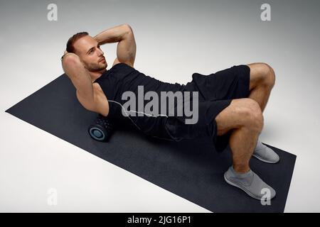 Man Foam Rolling. L'atleta si allunga utilizzando un rullo in schiuma. Foto Stock