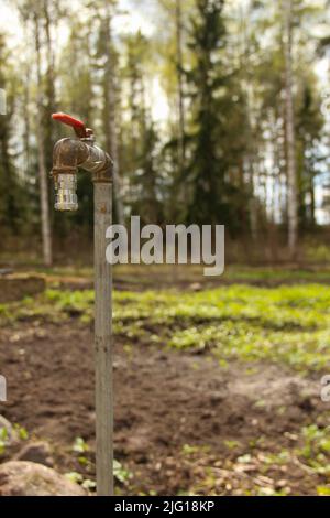 Un vecchio rubinetto d'acqua arrugginito in un giardino. Rubinetto giardino alla casa estiva. Foto Stock