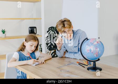 Gli allievi carini che guardano il globo in classe alla scuola. Ragazzo tenendo la lente d'ingrandimento e guardando la fotocamera Foto Stock