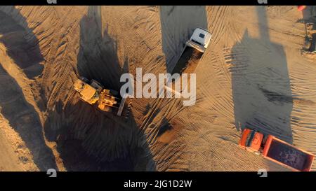 Vista dall'alto. Scene.i camion grandi su un terreno desertico vuoto riproducono i lavori di costruzione. Riprese a 4K° di alta qualità Foto Stock