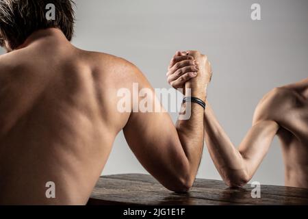Braccio wrestling. Braccio uomo pesante muscled bearded wrestling un uomo debole puny. Armi che lottano mano sottile, grande braccio forte in studio. Due mani dell'uomo aggrappate Foto Stock