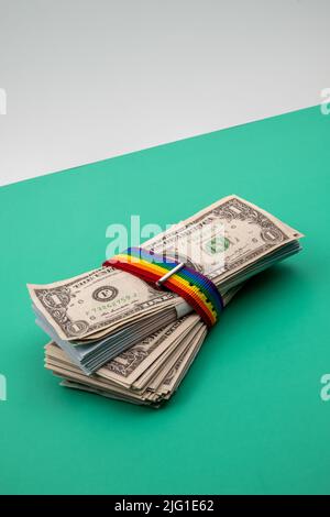 Primo piano di un pacchetto di bollette in dollari tenute insieme da una banda color arcobaleno sulla sommità di un tavolo verde con sfondo bianco. Foto Stock