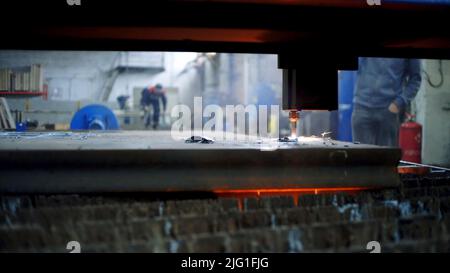 La macchina di fabbrica taglia il metallo. Clip. Primo piano della macchina per il taglio di metalli con scintille in fabbrica. Macchina di lavoro su sfondo sfocato con i lavoratori. Foto Stock