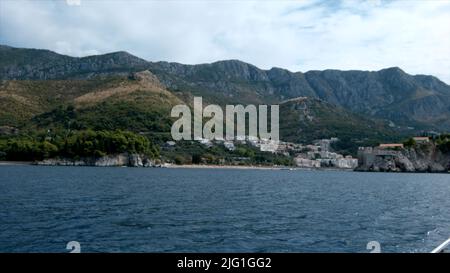 Vista dallo yacht su verdi colline tropicali e cielo nuvoloso. Creativa. Ondeggiante superficie del mare e verde riva con alberi e piante in crescita Foto Stock