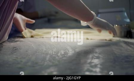 Primo piano di una mano in guanto mettendo la farina su un tavolo e una sfoglia di pasta. Clip. Processo di produzione di gnocchi in fabbrica Foto Stock