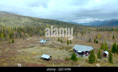 Concetto di turismo. Clip. Atterraggio in elicottero vicino alla solitaria casa in legno situata nella regione selvaggia con la valle e gli alberi Foto Stock