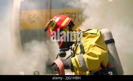 Vigile del fuoco maschile nei caschi e uniforme con fumo sullo sfondo. Clip. Pompieri preparazione tubo antincendio, concetto di emergenza Foto Stock