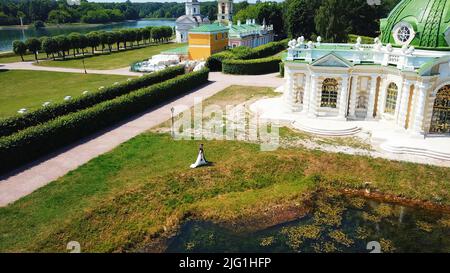 Vista aerea del parco cittadino in una soleggiata giornata estiva. Creativa. Parco con sposa a piedi in abito bianco e sposo, sentieri, alberi e erba verde Foto Stock