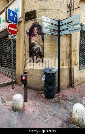 Un murale che raffigura il volto di una donna decora un edificio d'angolo su Rue Valedau a Montpellier, Francia; i cartelli indicano il Musée Languedocien, il Musée du Vieux Montpellier e il Musée Fougau, così come la Chapelle des Pénitents Blancs. Foto Stock
