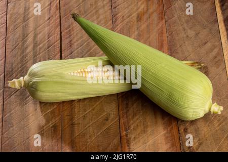 Zea mays - due pannocchie di mais fresche su sfondo di legno. Foto Stock