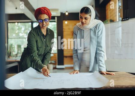 Architetti musulmani che lavorano su disegni blueprint in un ufficio moderno. Due imprenditrici creative che progettano un nuovo progetto innovativo. Donne designer wea Foto Stock