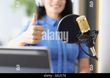 Donna in cuffie davanti al microfono in studio mostrando il pollice su segno Foto Stock