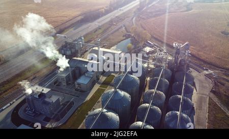 Volo aereo con vista sui droni sopra il complesso di edifici di ascensore di grano. Silos rotondi in metallo e barili in metallo per la conservazione dei cereali. Raccolta di stoccaggio in essiccazione. Serbatoi dell'elevatore e complesso di essiccazione della granella. Granaio grande Foto Stock