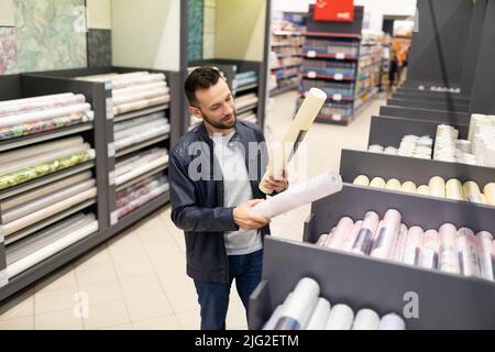 un cliente maschile in un negozio di materiali per la decorazione sceglie sfondi di carta Foto Stock