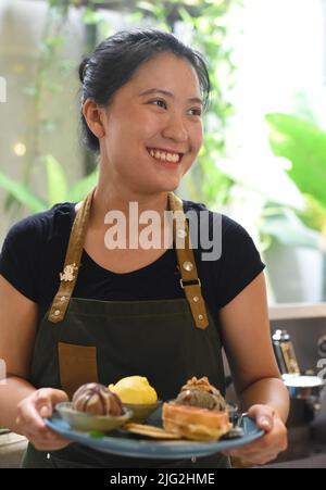 Ragazza vietnamita che serve gelato fatto in casa con waffle in una caffetteria. Foto Stock