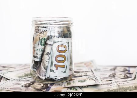 Vaso di vetro con monete su sfondo bianco. Un sacco di bollette in dollari. Foto Stock