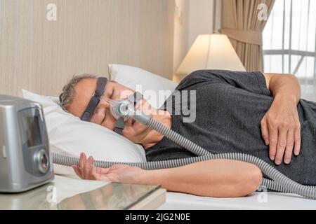 Maschio di mezza età con apnea del sonno indossando copricapo e maschera CPAP mentre dormiva nella sua camera da letto Foto Stock