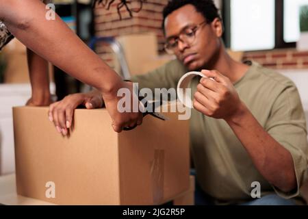 Partner sposati sigillare scatole di cartone con nastro adesivo per spostare mobili in nuova proprietà immobiliare. Imballando le cose e il carico di deposito di spedizione, godendo del trasferimento piatto. Primo piano. Foto Stock