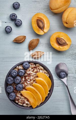 Colazione vegetariana. Fiocchi d'avena a grani interi con fette di albicocca e mirtilli. Vista dall'alto con spazio di copia Foto Stock